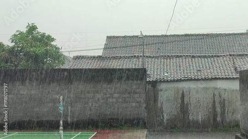 Heavy rain against a backdrop of walls and buildings in a rural setting.
