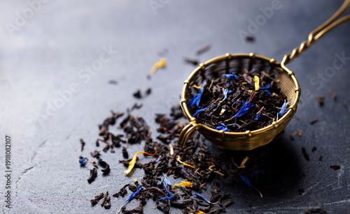 Earl grey loose leaf tea blend with cornflower and orange blossom petals in golden in brass wire tea strainer. Marble background. Close up. Copy space.
