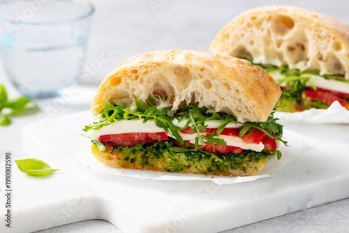 Bild auf Leinwand Ciabatta sandwich with mozzarella, tomatoes, pesto sauce and fresh basil on marble serving board