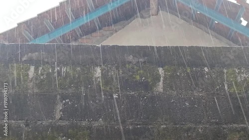 Heavy rain against a backdrop of walls and buildings in a rural setting.