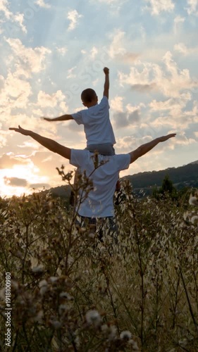Family happiness and outdoor activities. Man and boy with open arms against sunset sky.