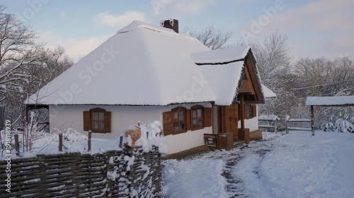 Snow-covered Ukrainian style house in a rural village during winter. Traditional wooden shutters, white walls and quiet countryside create a cozy seasonal atmosphere.