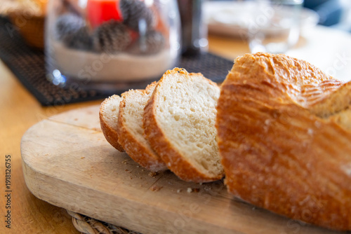 Partially sliced rustic loaf sitting on board on wood table, crumbs scattering, glass centerpiece
