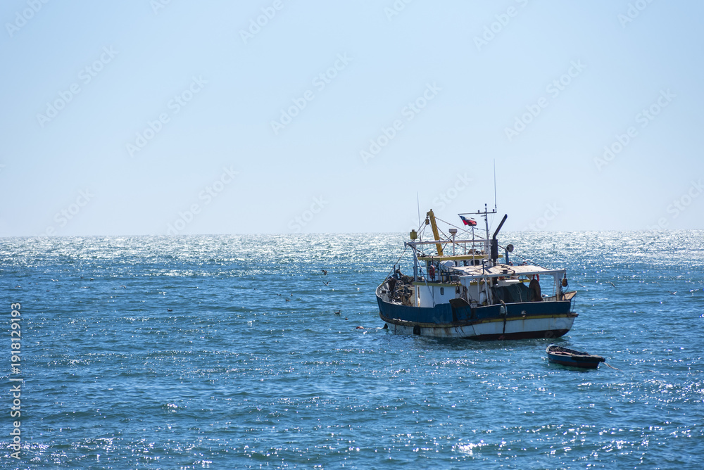Naklejka premium Peaceful maritime scene with a moored fishing boat facing the reflective waters of the Pacific Ocean in San Antonio, Chile.