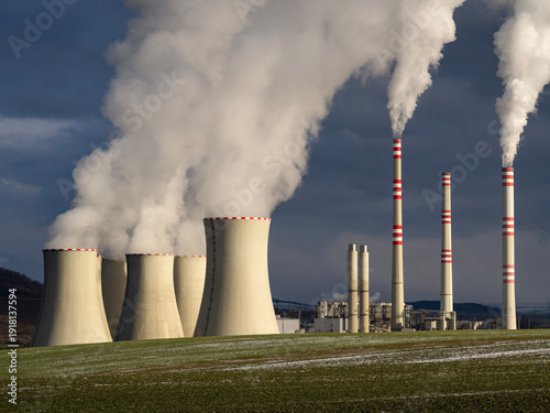 Coal-fired power plant with cooling towers and chimneys emitting thick steam and smoke against dark storm sky