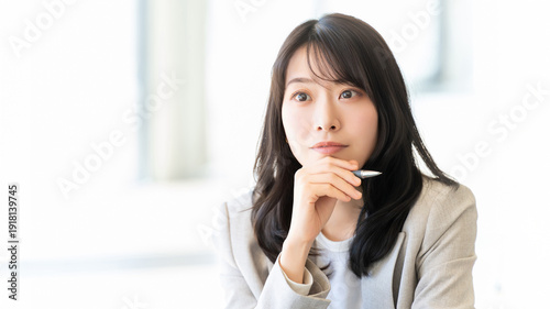 Foto ペンを持ち顎に手を当てて考える女性ビジネスパーソン, Businesswoman thinking with pen in hand