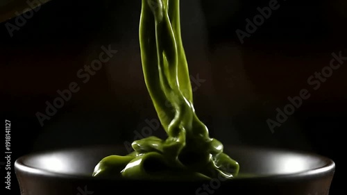 Close up of green liquid pouring in bowl in dark setting or Close up of substance flowing in bowl in dark setting