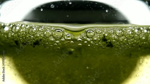 Close up of green liquid with bubbles rising in glass or Close up of bubbles forming on green liquid in container