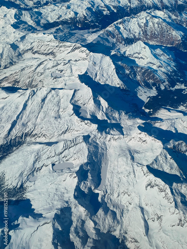 Aerial view from an airplane window of the snow-covered peaks of the Austrian Alps, showcasing a dramatic winter mountain landscape