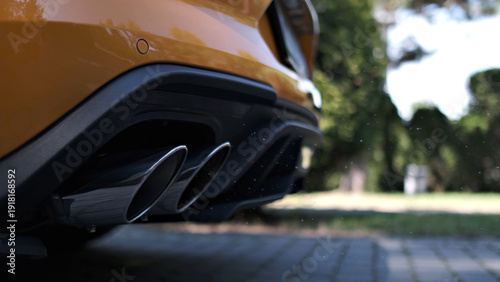 Schilderij op canvas Dual chrome exhaust pipes on a modern orange sports car rear bumper parked outdo
