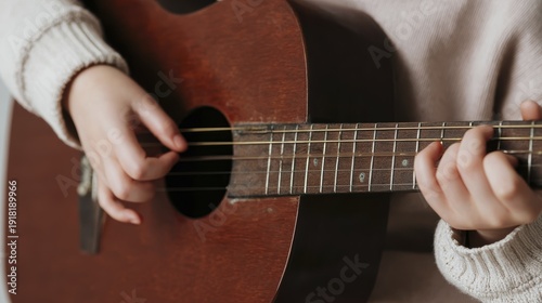 Child's hands strumming acoustic guitar strings in cozy home setting