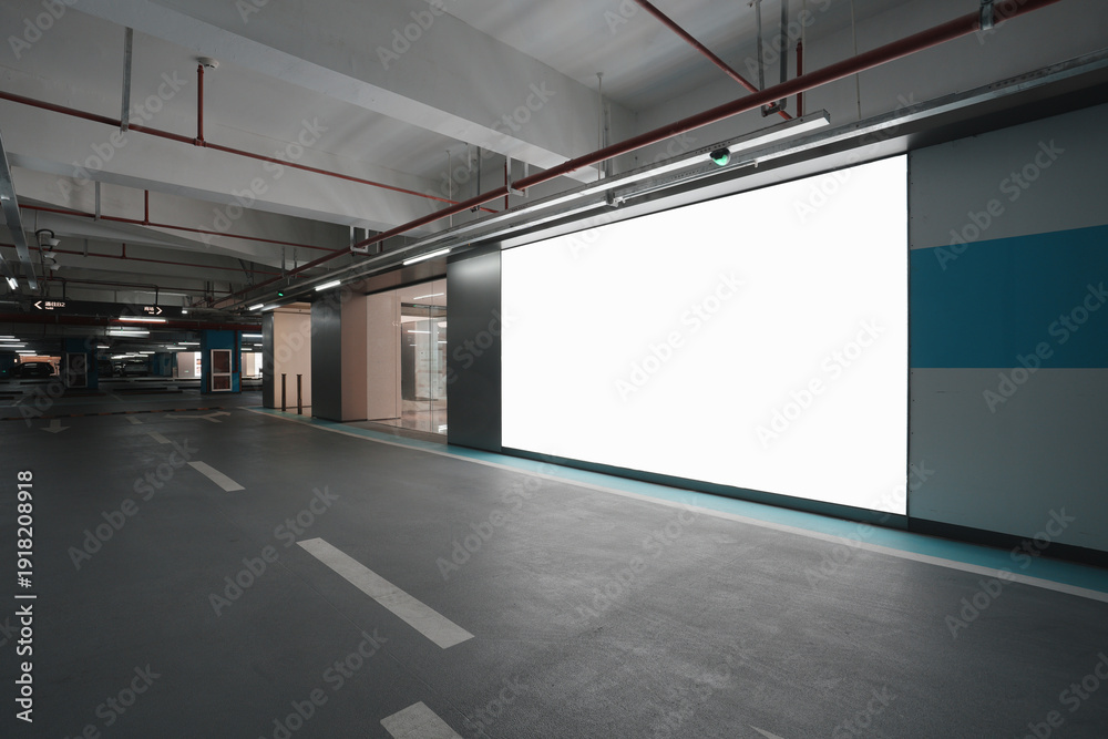 Obraz premium Underground parking garage with blank advertising wall and modern industrial lighting