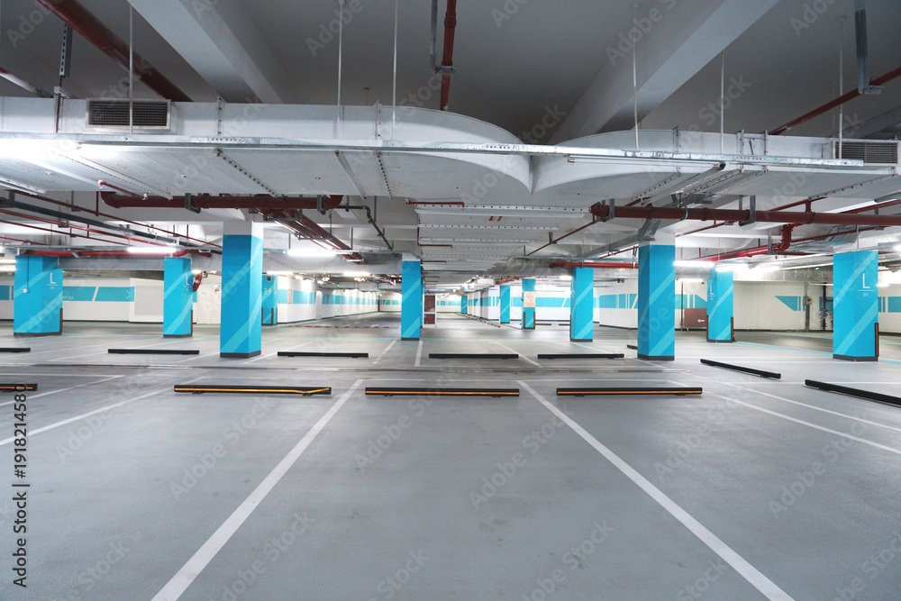 Fototapeta premium Empty underground parking lot with blue columns and marked parking spaces
