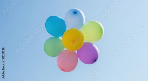 Seven brightly colored balloons cluster together forming a flower shape against a clear blue sky.