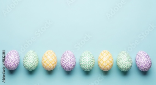 A row of eight patterned Easter eggs in soft purple, green, and yellow hues is lined up neatly along the bottom edge of a solid light blue surface.