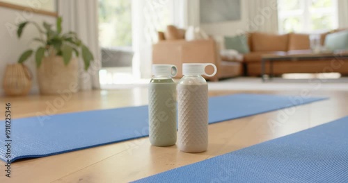 Camera is moving closer, raising angle, focusing two bottles on floor amid blue mats showing caps