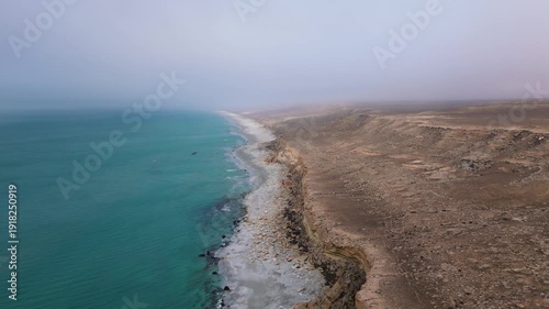 Aerial drone footage of a long sandy coastline in Aktau, Mangystau, Kazakhstan, bordered by low cliffs on one side and the Caspian Sea on the other. Empty rocky beach and vast open space create 