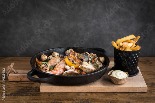 Photos A seafood stew in a pan on a wooden plank with fries and mayonnaise on a wooden