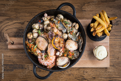 Photos A seafood stew in a pan on a wooden plank with fries and mayonnaise on a wooden