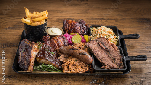 A barbecue meat platter with spare ribs, pulled pork, sausage, beef brisket slices, coleslaw, fires, mayonnaise, chicken pieces and pickles