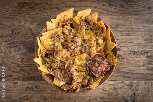 Nachos loaded with pulled pork and cheese with a salsa dip in a bowl on a wooden table