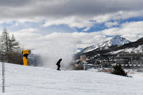 Skiers and snowboarders descending a ski slope in an Italian ski resort. People skiing down a wide snowy piste overlooking Sestriere town in the Piedmont region. Winter holiday resort in the mountains