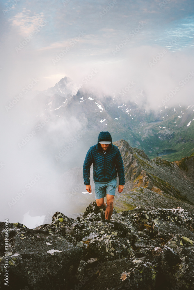 Obraz premium Active man hiker climbing foggy mountains travel in Norway healthy lifestyle extreme vacations in Lofoten islands adventure tour outdoor, traveler mountaineering solo endurance and freedom in the wild