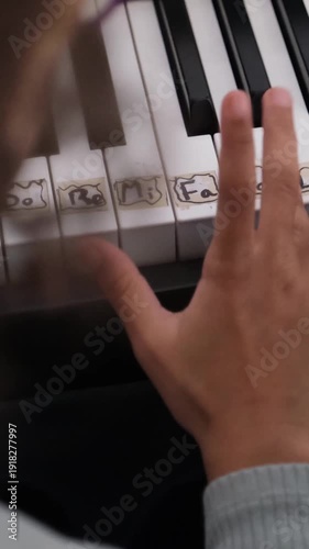 Close up view of a young child's hand learning to play the piano. Kid's fingers pressing the white keys with solfege notes written on them
