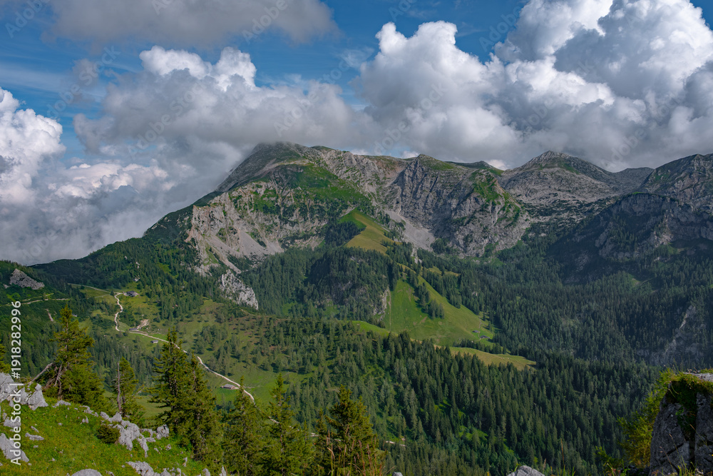 Obraz premium Mountain covered in green forest illuminated by warm summer sun through clouds