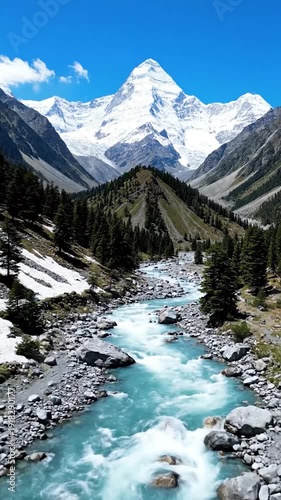 A clear river flows through a mountain valley towards a snow-capped peak.