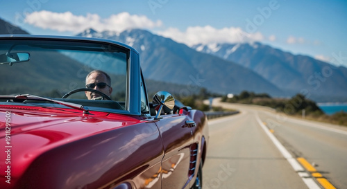 Man drives classic convertible road trip on highway, lake and mountains background. Vintage red car offers freedom, driver enjoys memorable convertible road trip.