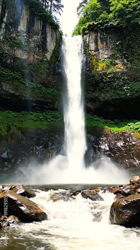 Powerful waterfall cascades down a y cliff surrounded by lush green forest