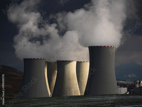Massive cooling towers of power plant emitting thick steam against dark dramatic storm sky