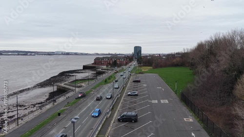 Aerial tracking shot of traffic on a Liverpool shoreline road with promenade and low‑tide mudflats.