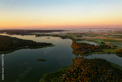 Wallpaper Mural Aerial sunrise over Masurian Lakeland in Poland, mist drifting above calm lakes and patchwork fields, golden morning light illuminating forests and rural landscape with wind turbines Torontodigital.ca