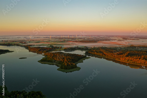 Wallpaper Mural Aerial sunrise over Masurian Lakeland in Poland, mist drifting above calm lakes and patchwork fields, golden morning light illuminating forests and rural landscape with wind turbines Torontodigital.ca