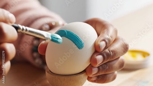 Hands painting an egg with a small brush.