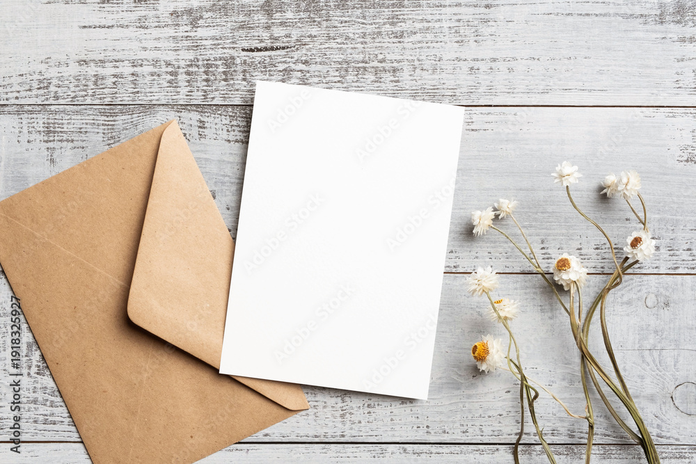 Fototapeta premium Blank invitation card mockup with envelope, dried flowers decoration on wooden background, card with copy space for design presentation