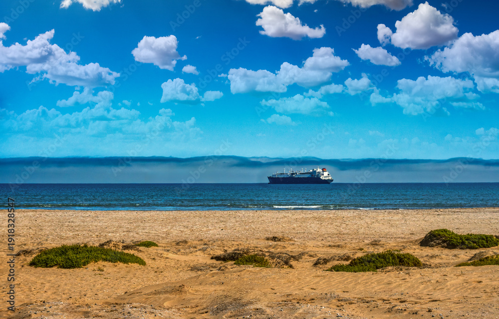 Obraz premium Cargo ship and coastal fog over the Skeleton Coast, Namibia. Bright blue sky with scattered clouds