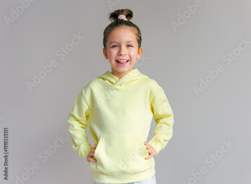 Cute little girl wearing blank yellow hoodie. Grey background. Mock up template for design