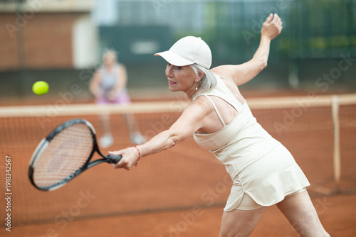 Konstfotografi Rear view of emotional aged woman enthusiastically playing tennis outdoors in su