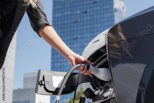 Photos Woman charging electric car at the charging station near city skyscraper