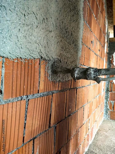 Construction worker applying cement plaster coating to a wall using a machine. Machine Plastering, process involves a plastering machine that sprays mortar onto surfaces to achieve a smooth and consis