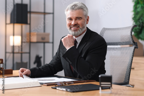 Canvastavla Portrait of smiling notary in suit with documents at table in office