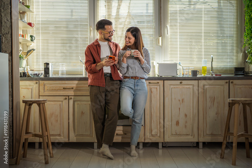 Obraz na płótnie Couple enjoying morning coffee and smart phone in kitchen