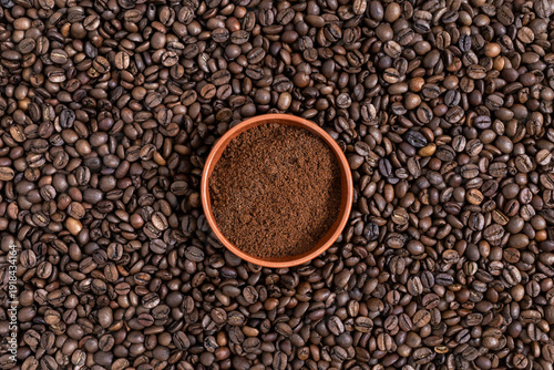 Top view of a small clay bowl filled with fresh ground coffee powder on a textured background of roasted beans. Flat lay centered composition, copy space