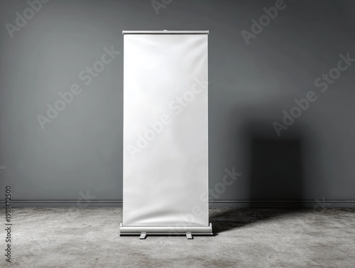 A vertical, blank, white retractable banner display stands in front of a shadowed, gray-walled space with a concrete floor
