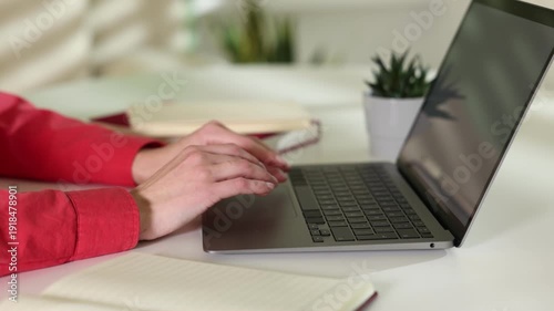 Woman working on laptop at white table indoors, closeup