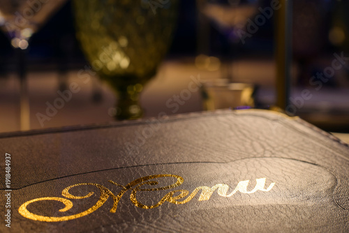Canvas Print Closeup leather bound menu with golden shiny letters at restaurant table
