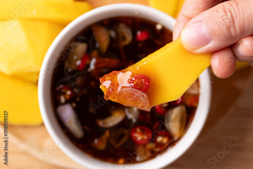 Close up of hand dipping sliced mango into Thai sweet fish sauce (Nam Pla Wan)